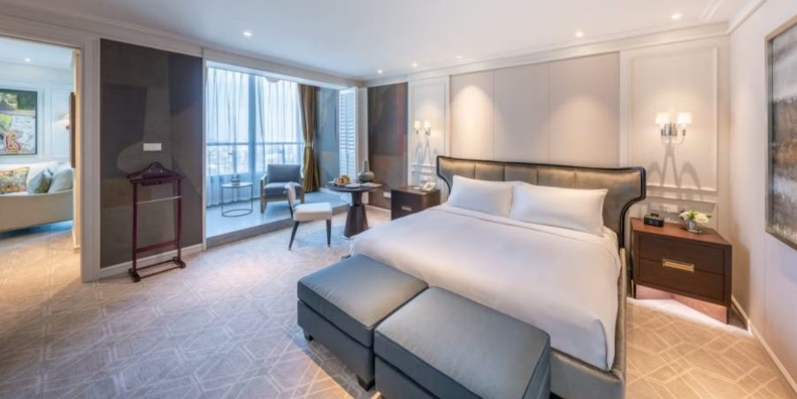 A spacious hotel room with a king-size bed and a large window, offering a bright and inviting atmosphere.